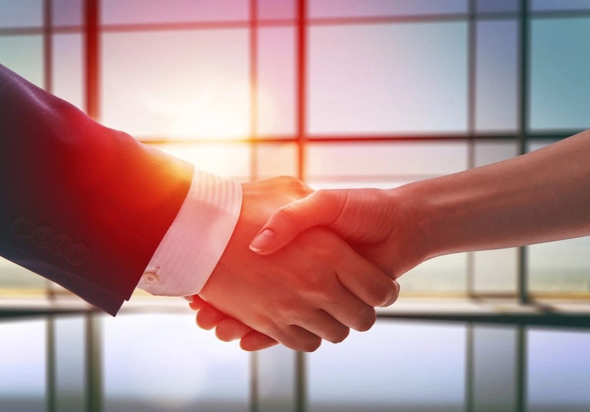 Two people shaking hands in front of a window.